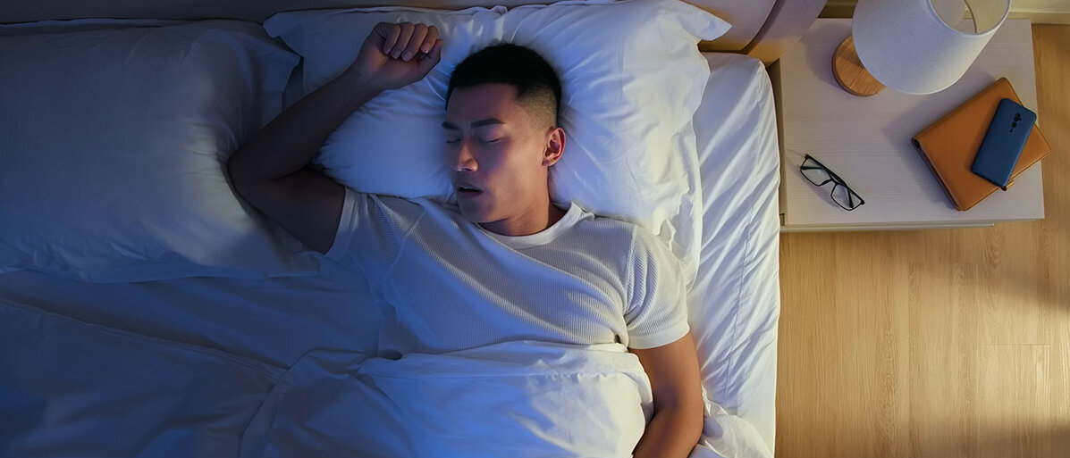 Mann schläft mit offenem Mund im Bett.