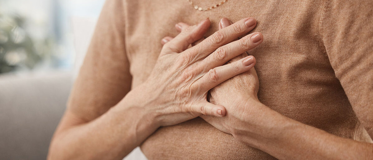 Vorboten eines Herzinfarkts kennen. Eine nicht zu erkennende ältere Frau hält sich beide Hände an die Brust.