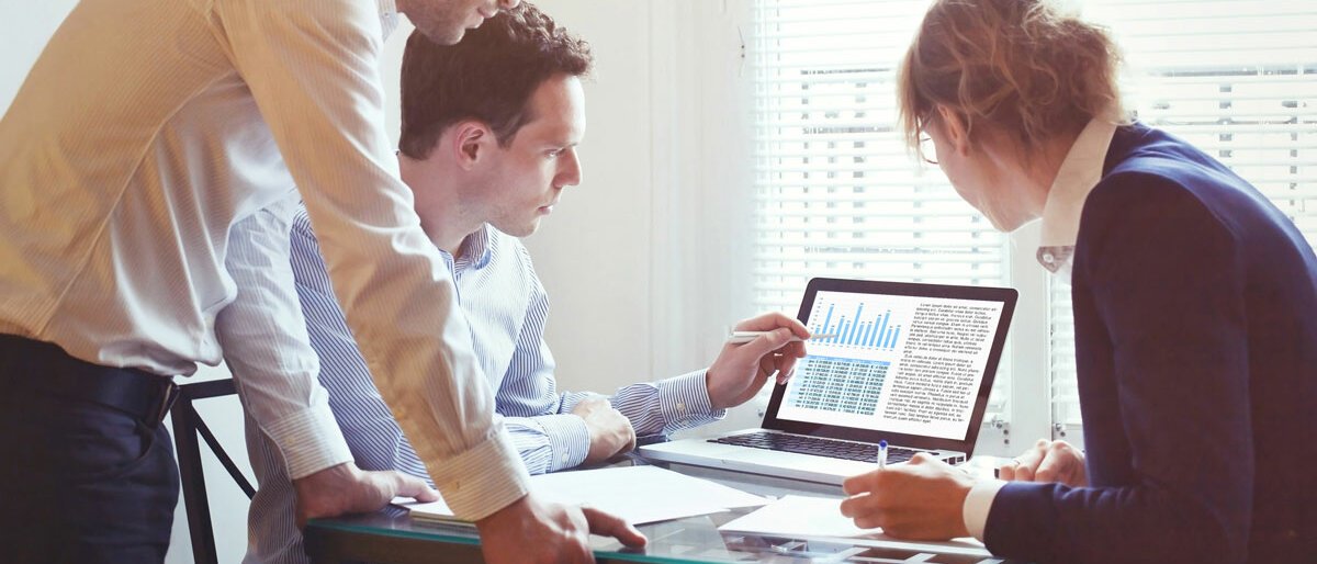 Drei Menschen schauen sich Statistiken auf einem PC an