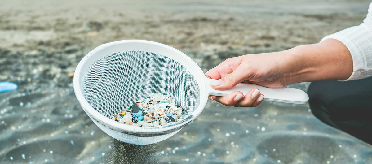 Eine Frau reinigt Wasser und Sand mit Hilfe eines Siebs von Mikroplastik