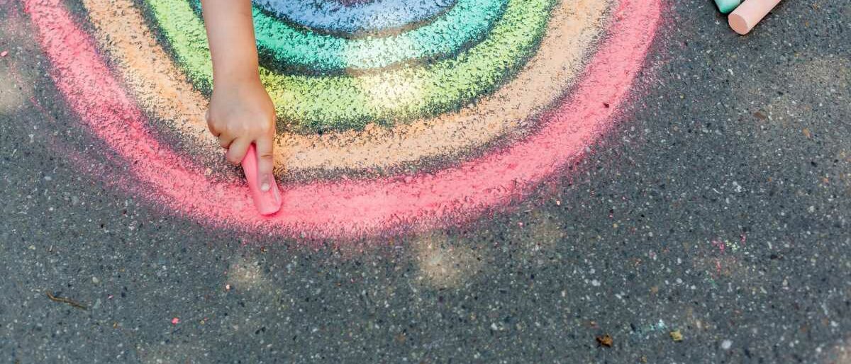 Ein Kind malt mit Kreise einen Regenbogen auf Asphalt.