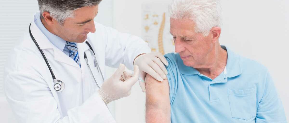 Ein Arzt impft einen weißhaarigen Senioren in den Oberarm.