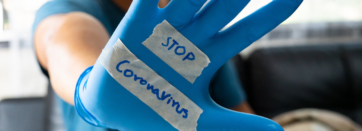 Eine blau behandschuhte Hand mit der Aufschrift: Stop Coronavirus