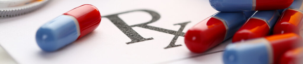 Das Wort Rx steht auf einem Blatt Papier, auf dem ein paar Kapseln liegen