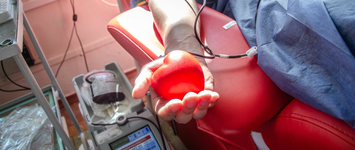 Eine Person beim Blutspenden hält ein rotes Schaumstoffherz in der Hand