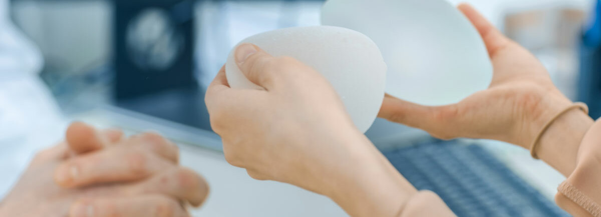 Ein Arzt zeigt einer Frau zwei Brustimplantate, sie hält diese in den Händen