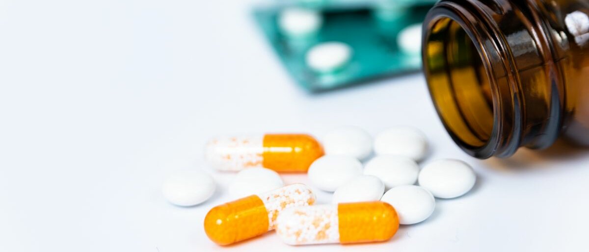 Arzneimittel Eine umgekippte Medikamentendose, aus der Pillen fallen, liegt auf weißem Untergrund.