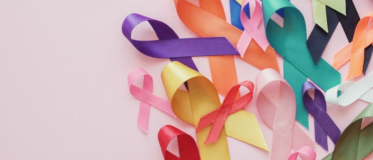 Bunte Bänder liegen auf rosa Hintergrund, um auf Krebserkrankungen aufmerksam zu machen.