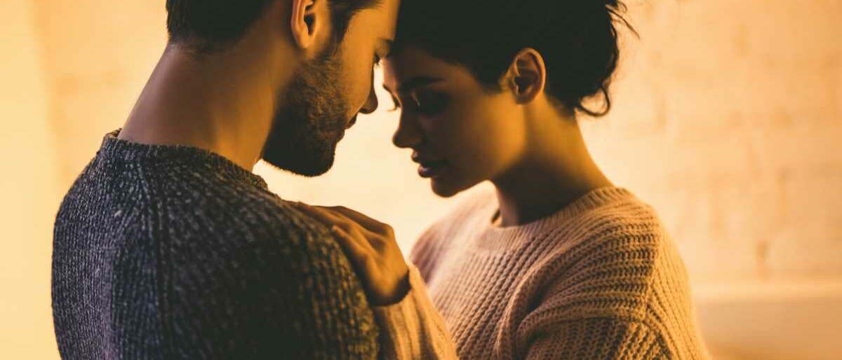 Ein Mann und eine Frau in kuschligen Pullovern stehen sich sehr nah gegenüber.