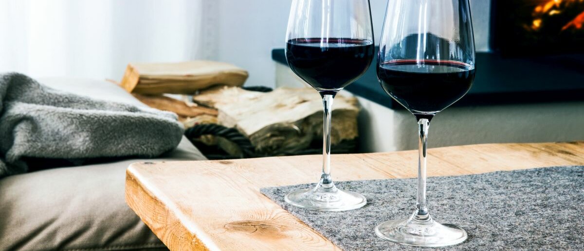 Nahaufnahme von zwei Gläsern mit Rotwein auf dem Tisch im Wohnzimmer mit Kamin im Hintergrund.