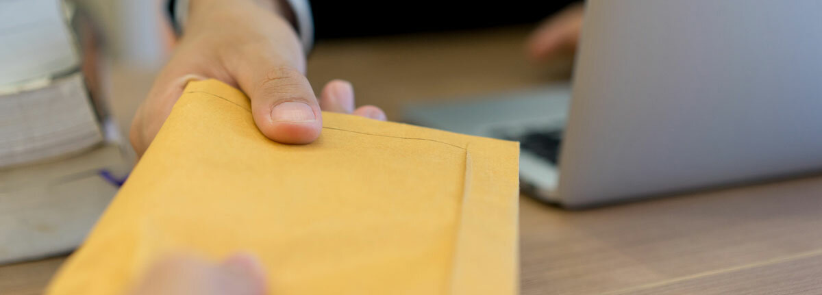 Jemand erhält einen orange-farbenen Umschlag und sitzt hinter einem Laptop