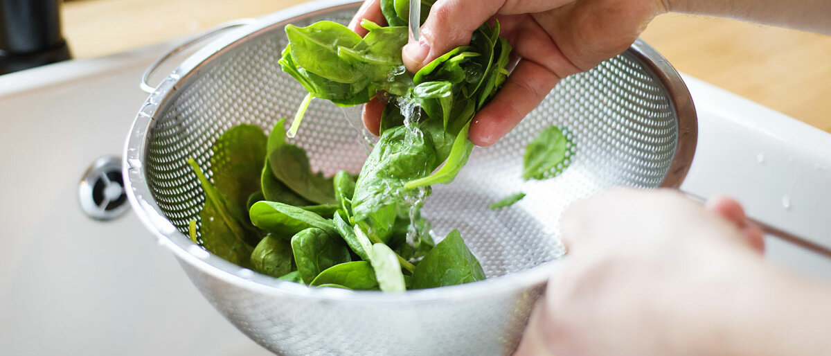 Jemand wäscht Feldsalat in einem Sieb unter einem Wasserstrahl