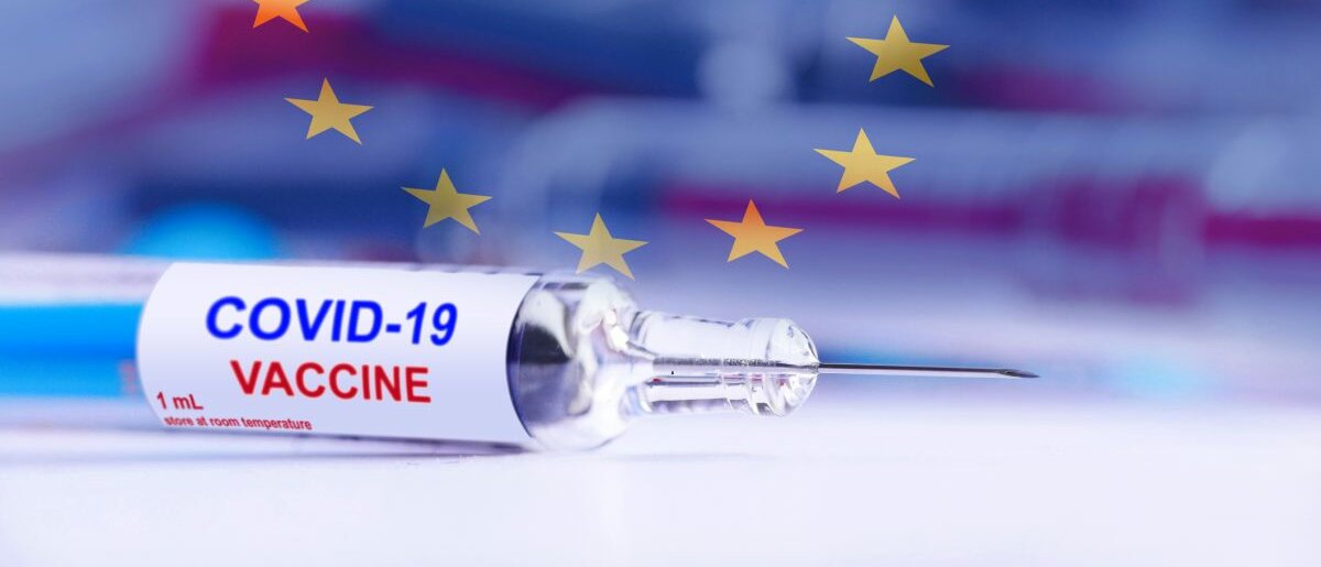 Ein Corona-Impfstoff auf einer glatten Fläche und einer Europa-Flagge im Hintergrund.