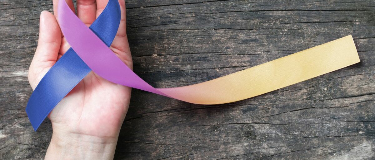 Harnblasenkrebs Eine Hand hält die farbige Schleife in der Hand, die symbolisch für das Blasenkrebs-Bewusstsein steht.