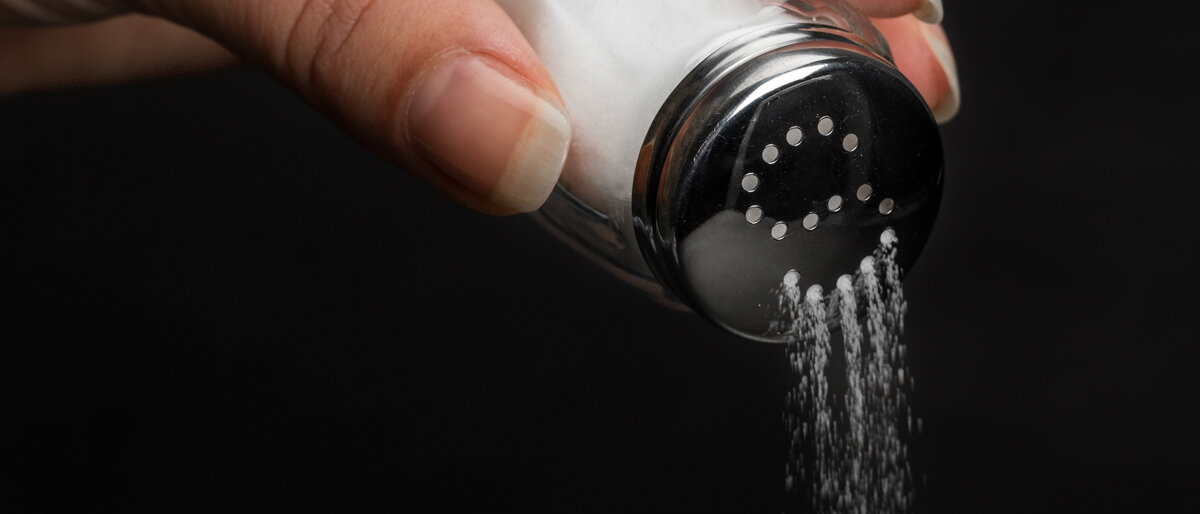 Hand streut Salz auf Essen mit Streuer