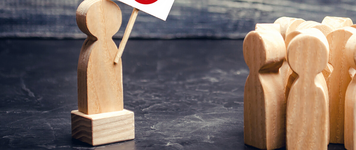 Ein Holzmännchen hält vor einer Gruppe weiterer Holzmännchen ein Verbotsschild hoch.