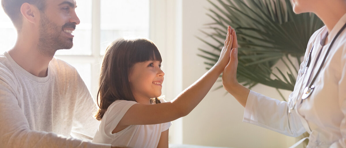Ein junger Mann ist mit einem Mädchen beim Arzt, das klatscht gerade mit einer Ärztin ab