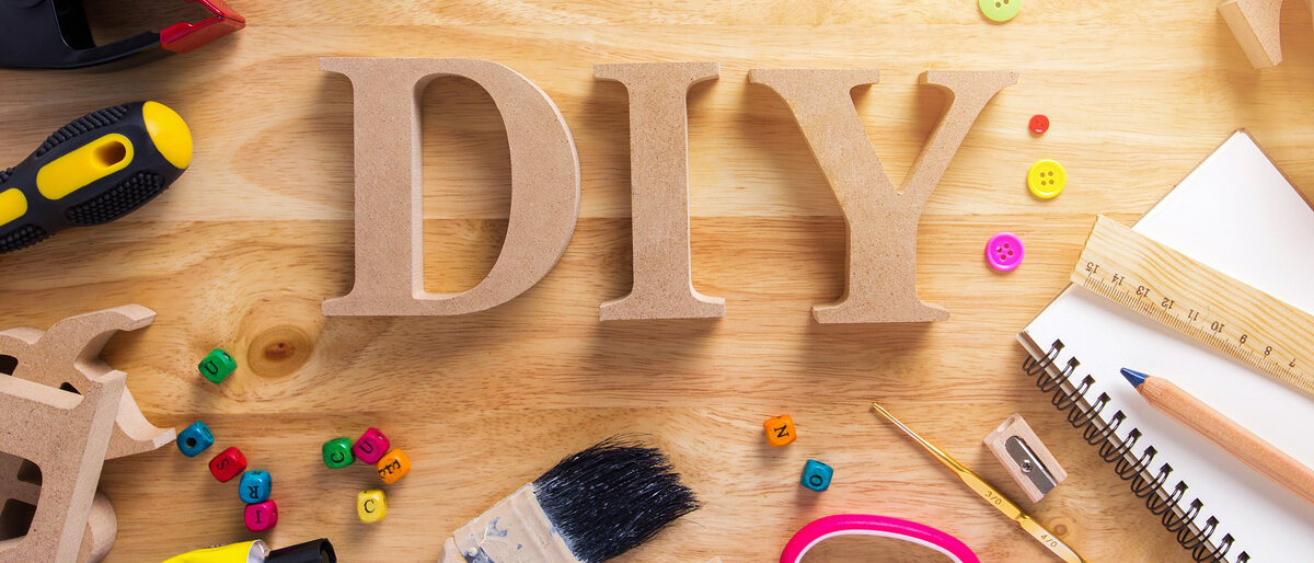 Das Wort DIY in Holzbuchstaben, drum herum Schere, Bastelutensilien, Kunstbedarf