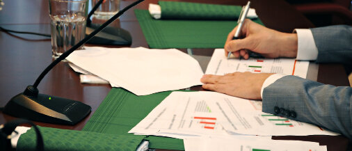 Nahaufnahme einer ABDA-Sitzung mit Dokumenten, Mikrofonen und Teilnehmenden beim Auswerten von Diagrammen. 