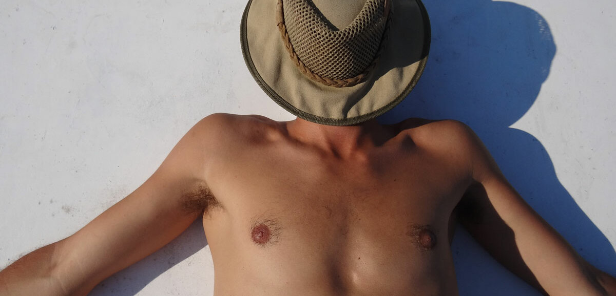 Ein Mann liegt, mit einem Sonnenhut über dem Gesicht, in der prallen Sonne am Strand.