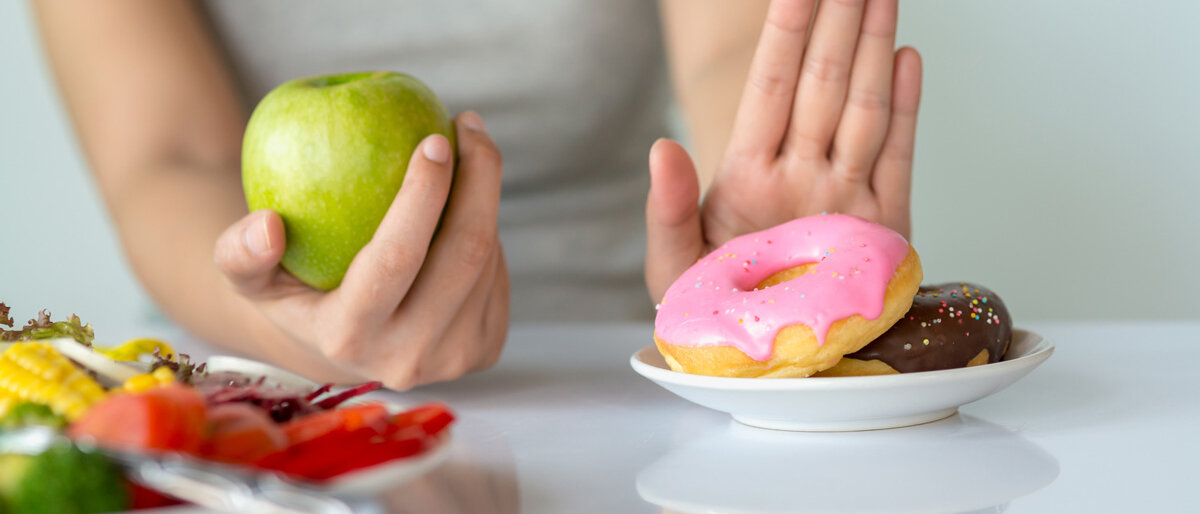 Fasten Die linke Hand greift nach einem Apfel, die rechte wehrt Donuts ab.
