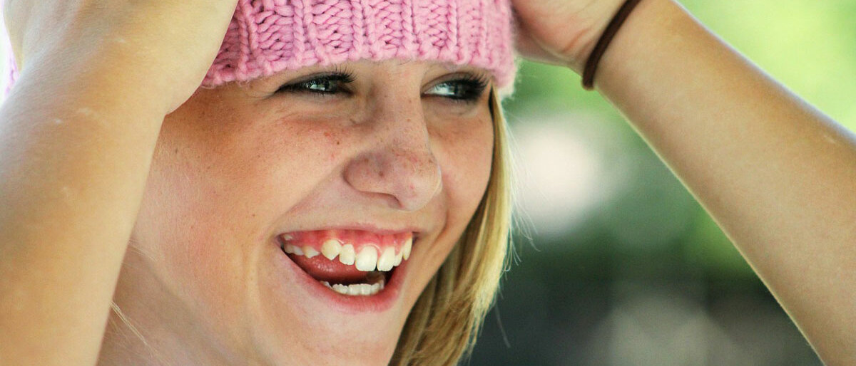 ein lachendes Kind zieht sich seine rosa Wollmütze runter