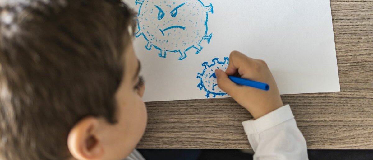 Ein Kind, das Coronaviren mit bösem Gesichtsausdruck malt aus der Vogelperspektive.