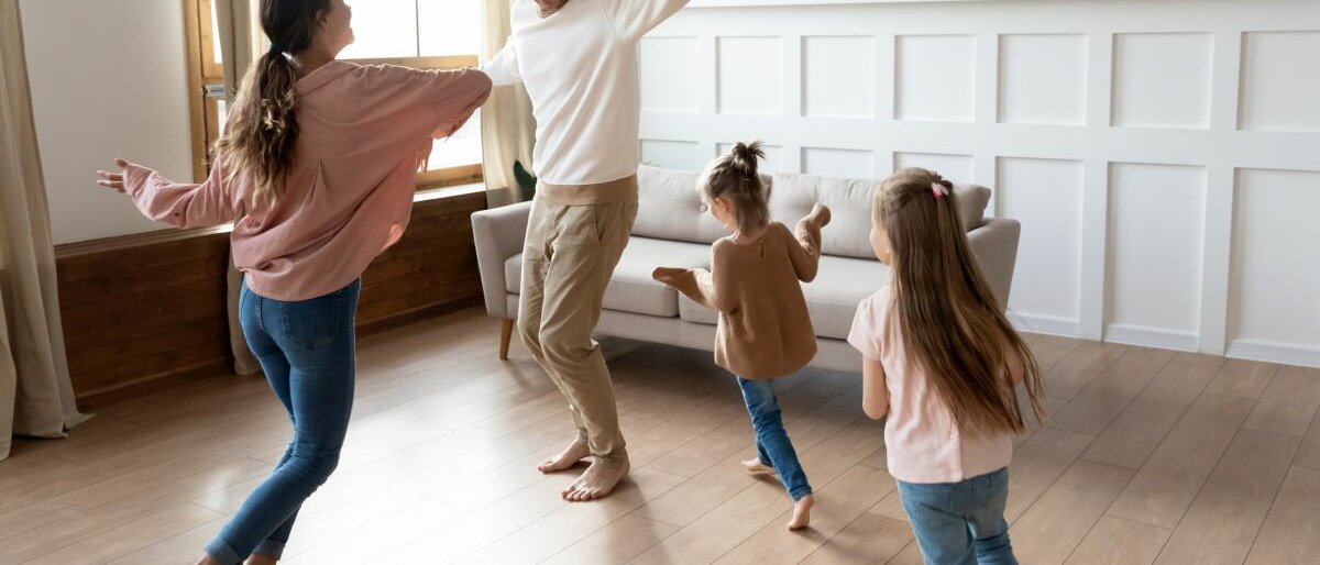 Mutter und Vater tanzen mit ihren zwei Töchtern durch einen Raum.