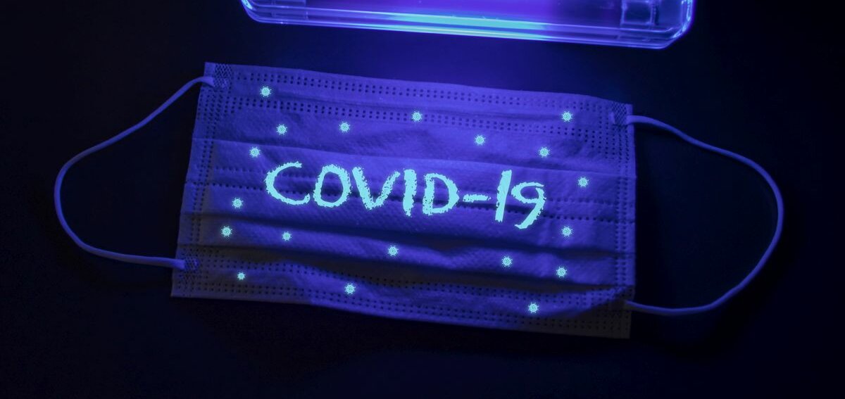 Eine Atemschutzmaske auf der "COVID-19" steht im UV-Licht.