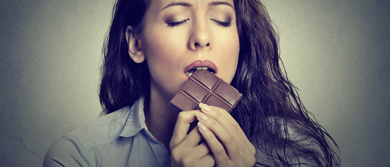 Frau beißt in Schokoladentafel. © SIphotography / iStock / Getty Images Plus