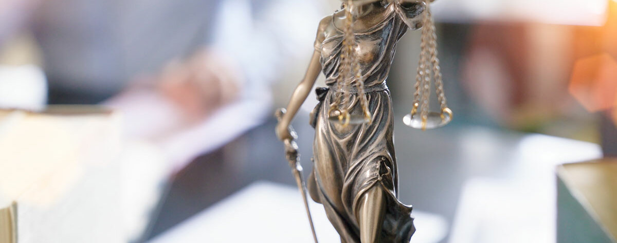 Justitia Eine Statue der Göttin Justitia hält mit verbundenen Augen eine Waage mit Waagschalen.