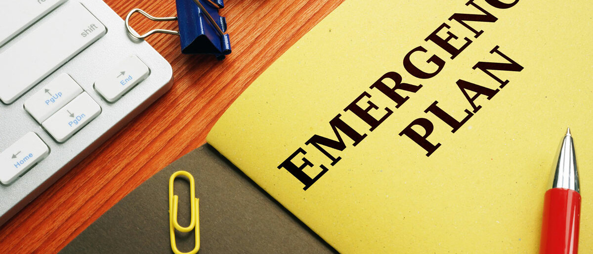 Katastrophenplan Ein Schreibtisch, auf dem eine gelbe Mappe mit der Aufschrift Emergency Plan liegt