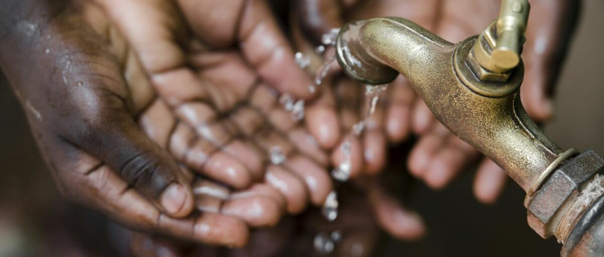 Hände fangen fließendes Wasser von einem Wasserhahn auf.