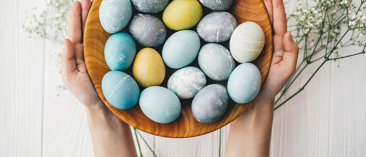 Viele blassbunt gefärbte Eier liegen in einer Holzschale, die mit zwei Händen gehalten wird.