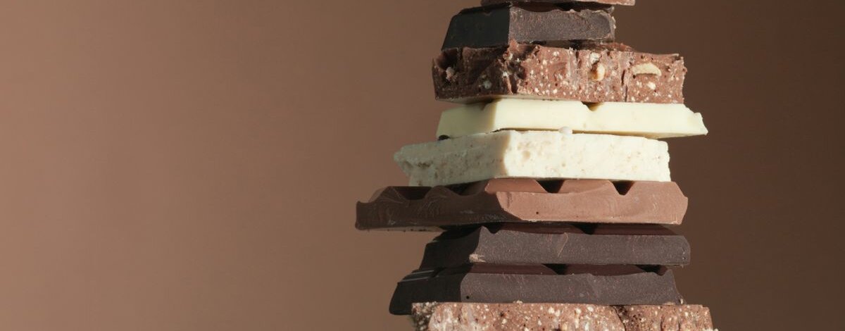 Verschiedene Schokoladensorten übereinandergestapelt vor braunem Hintergrund.
