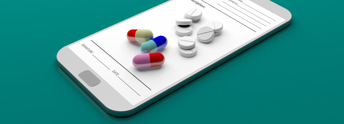 Auf einem Smartphone wird ein Rezeptformular angezeigt sowie Tabletten und bunte Kapseln.