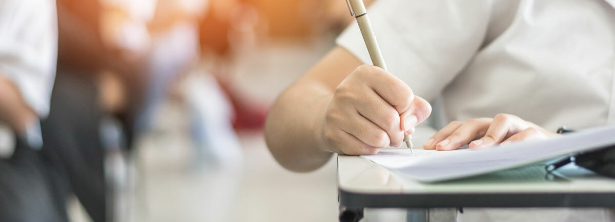 Eine Schülerin in weißer Bluse schreibt in der Schule mit