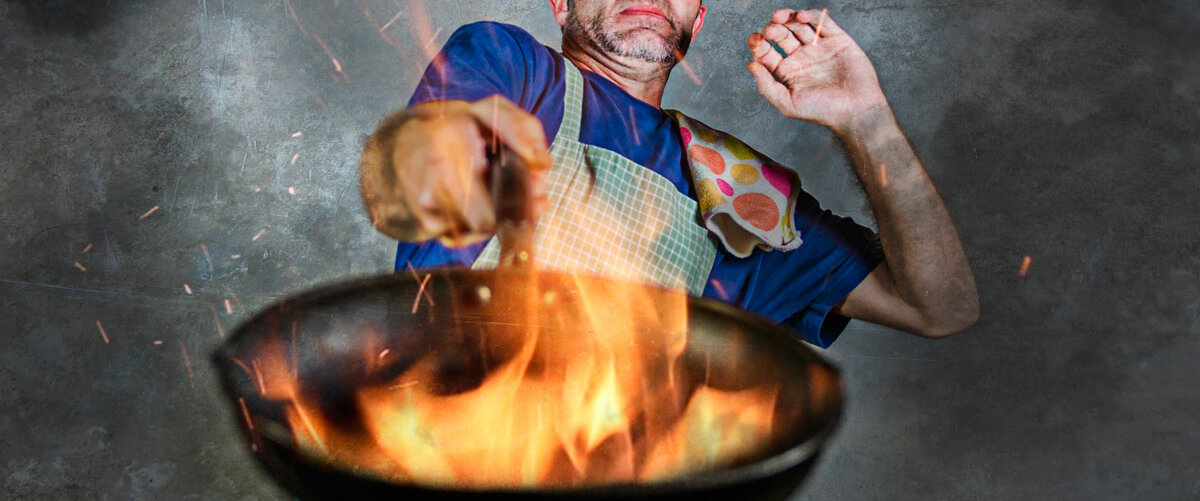 Ein Mann hält panisch einen brennenden Wok hoch
