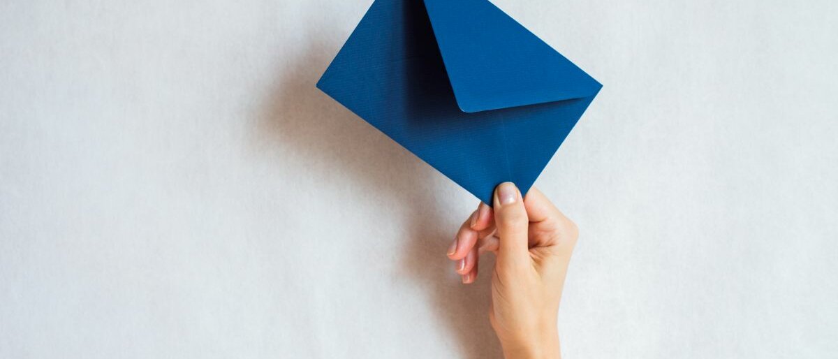 Eine Hand hält einen blauen Briefumschlag hoch.