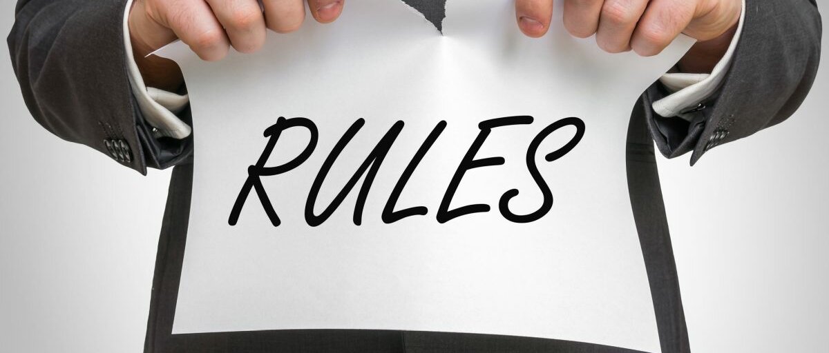 Ein Mann im Anzug hält ein Blatt mit der Aufschrift "Regeln" in der Hand und zerreißt es in der Mitte.