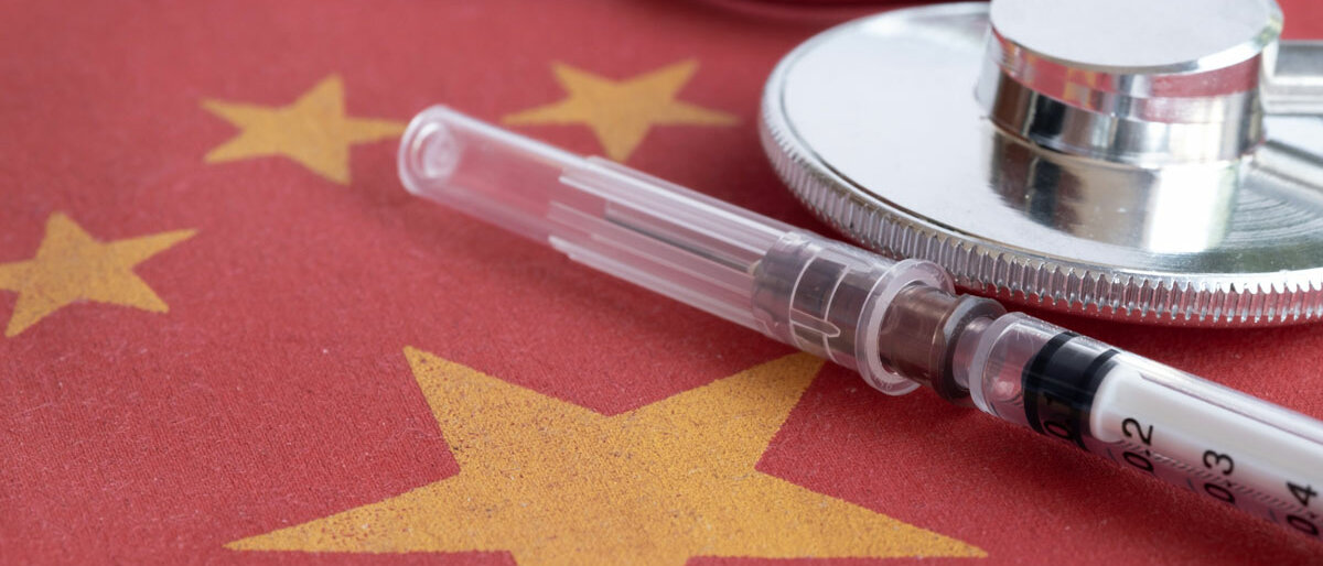 Auf einer chinesischen Flagge liegen eine Spritze und ein Stethoskop.