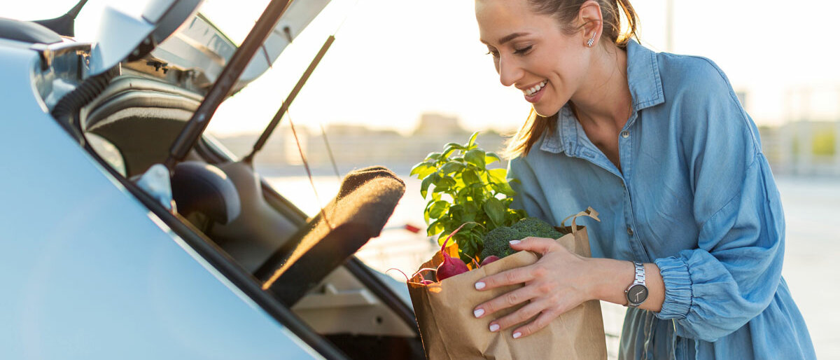Eine Frau holt aus ihrem Kofferraum eine Einkaufstüte mit Obst und Gemüse