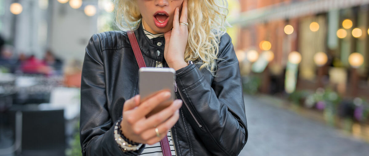 Eine junge Frau schaut auf ihr Smartphone und schaut schockiert.