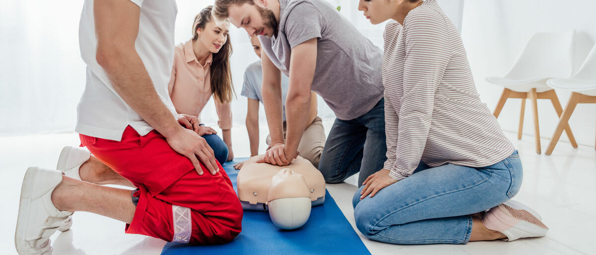 Sanitäter und Teilnehmer eines Ersthelfer-Kurses knien um eine Puppe, an der man Wiederbelebung üben kann.