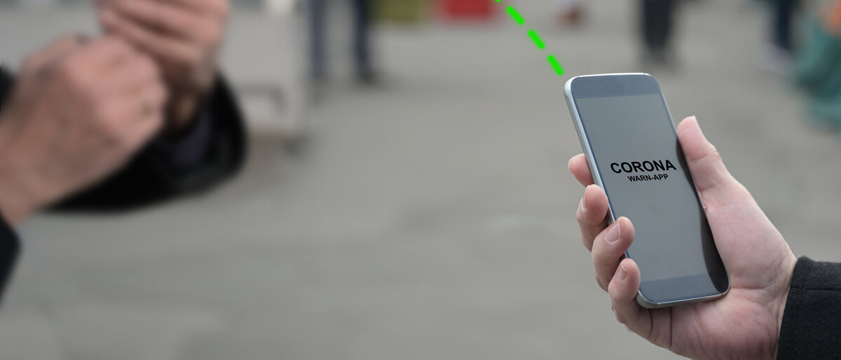 Zwei Personen halten ihre Smartphones in der Hand, auf dem Display sieht man die Corona-Warn-App. Die Handys tauschen angedeutet Informationen aus.
