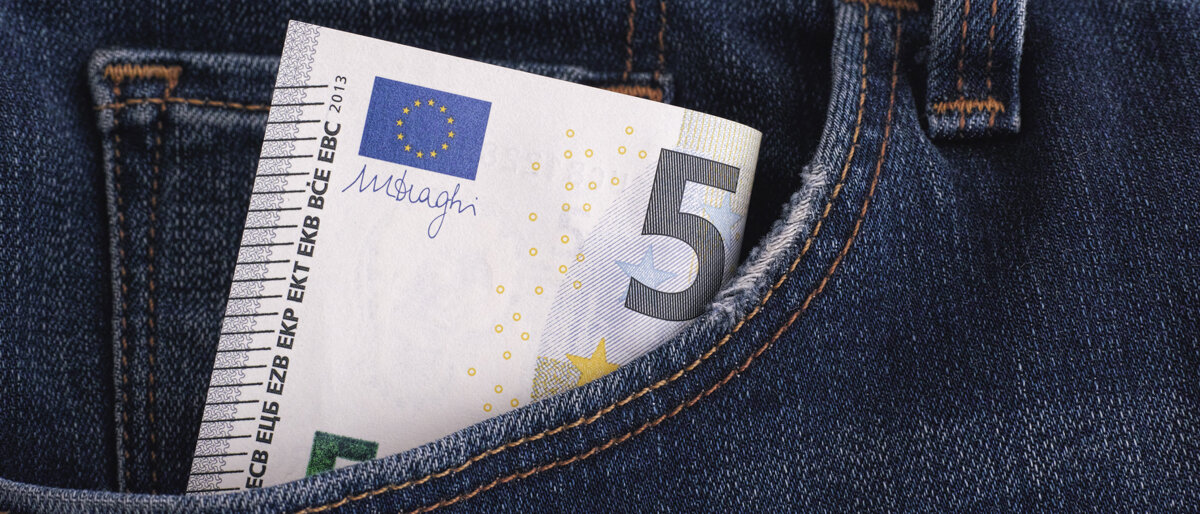 Ein Fünf-Euro-Schein schaut aus einer Hosentasche heraus.