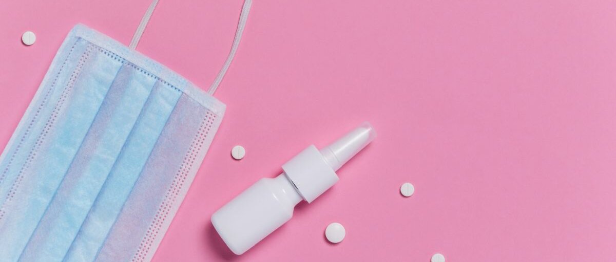 Nasenspray Nasenspray, Tabletten und eine Mund-Nasen-Maske auf pinkem Untergrund.