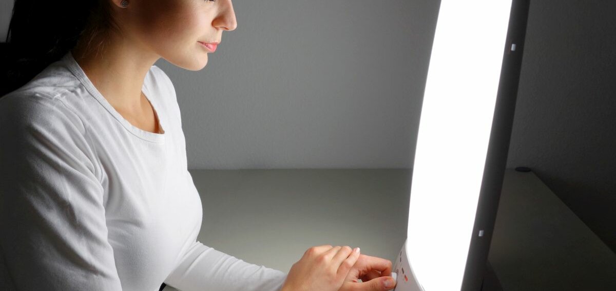 Lichttherapie Eine Frau sitzt vor einer lichttherapeutischen Lampe.