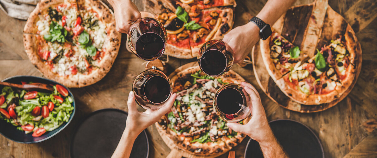 Menschen stoßen mit Wein an und essen Pizza.