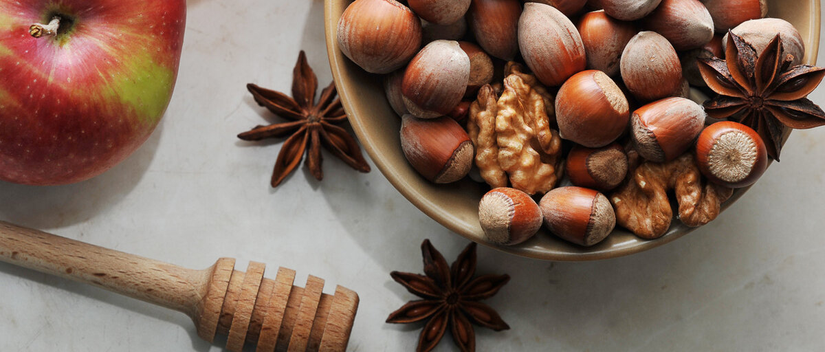 Äpfel, Nüsse und Gewürze auf hellem Untergrund.